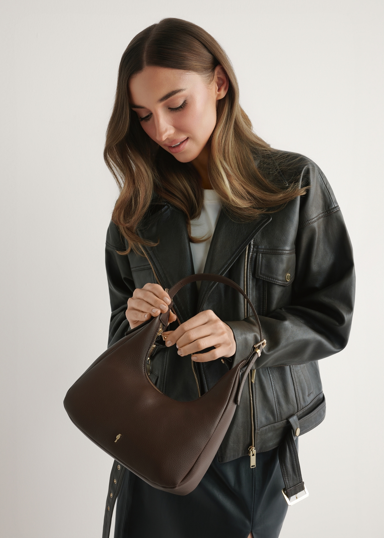 Small brown women's handbag TOREC-1239-1I(W26) - front view of the product, held by the model, against a light background. Half of the silhouette is visible.