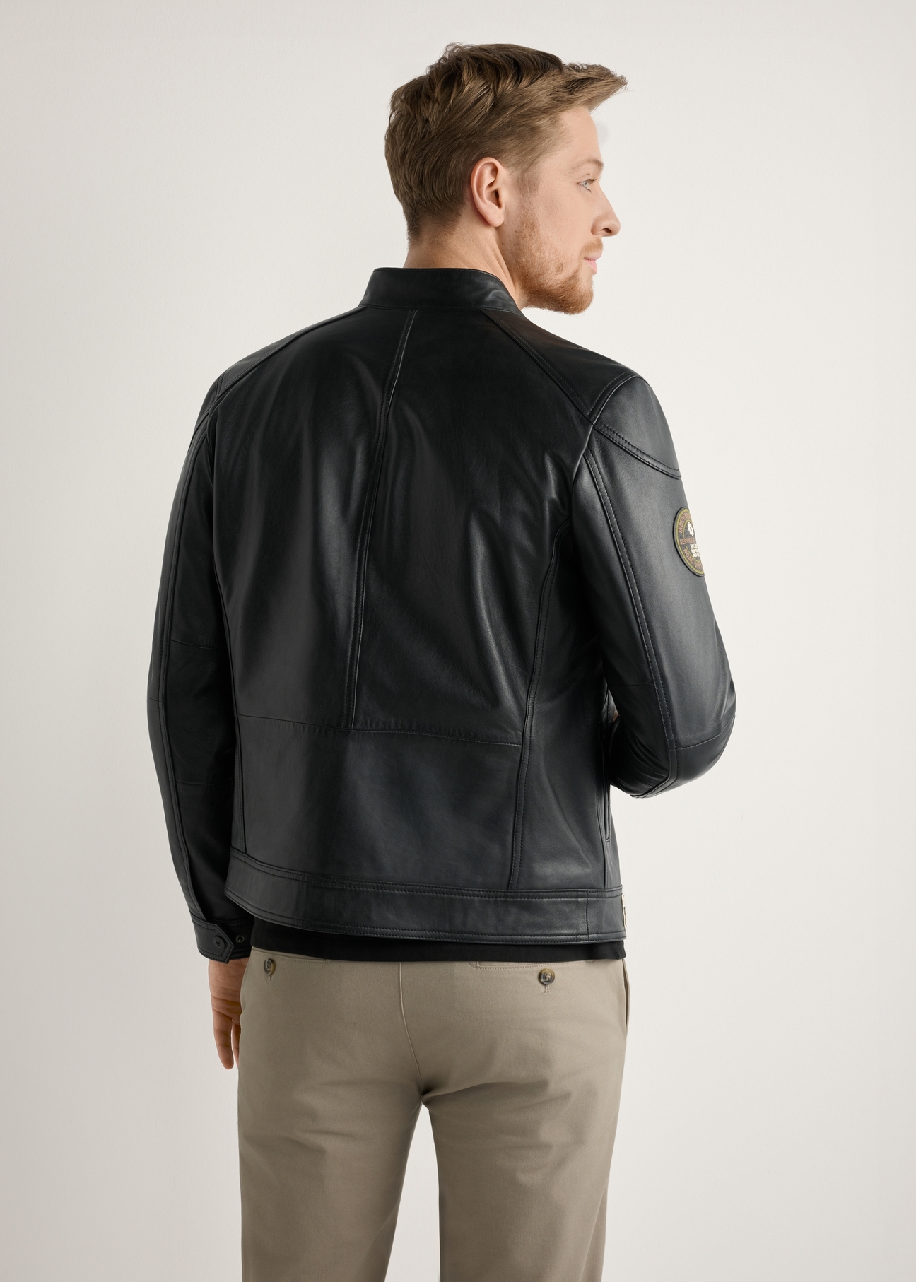 Skórzana czarna kurtka męska KURMS-0301A-99(W26) - widok produktu z tyłu, na modelu, na jasnym tle. Widoczna połowa sylwetki. 