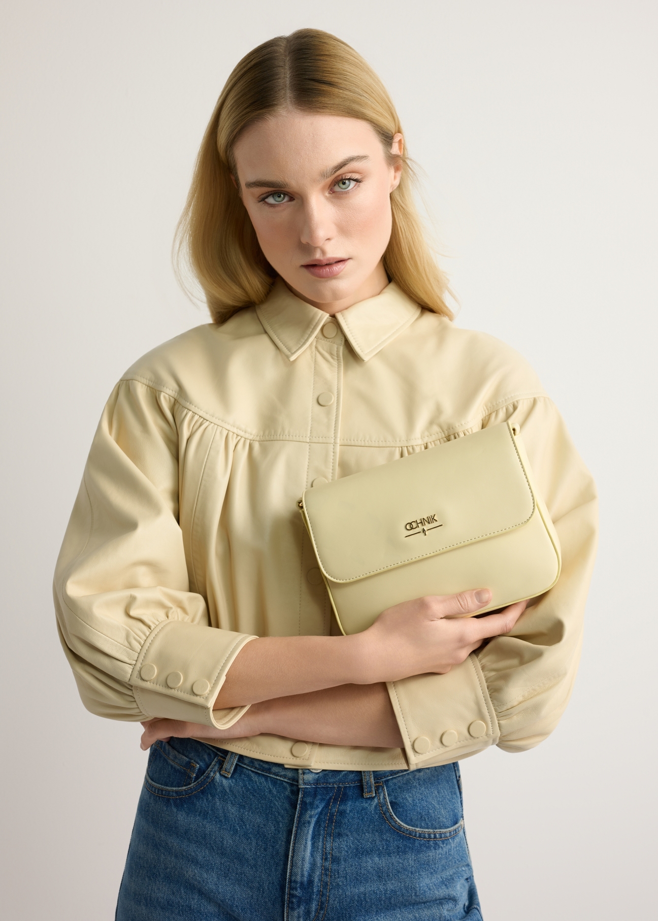 Light yellow women's messenger bag with chain TOREC-0767-2A(W26) - front view of the product, held by the model, against a light background. Half of the silhouette is visible.