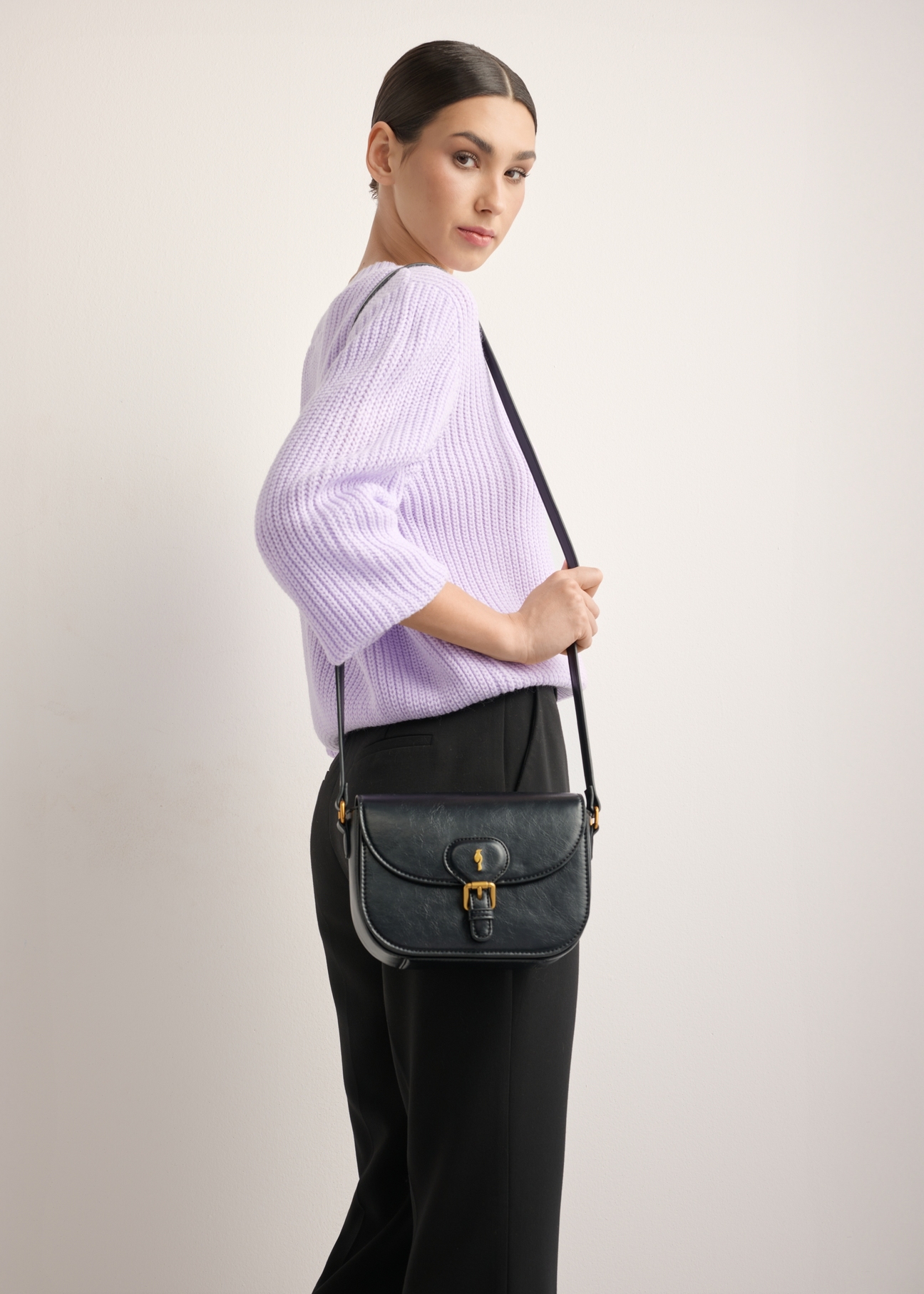 Small black women's messenger bag with decorative clasp TOREC-1243-9F(Z26), front view on model. Full body visible.