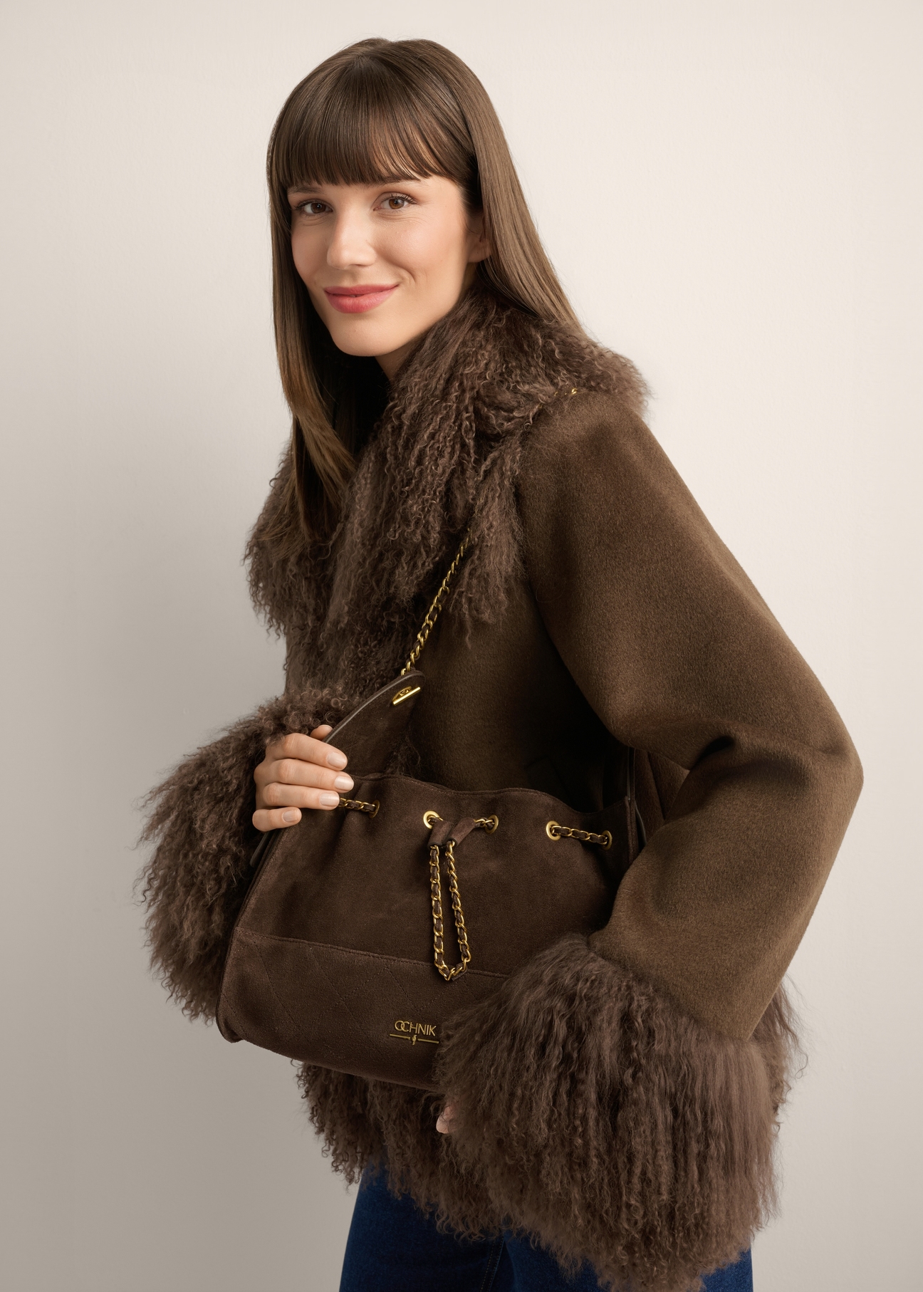Medium brown suede women's handbag TORES-1408-1I(Z26) - front view of the product, held by the model on her shoulder, against a light background. Half of the silhouette is visible.