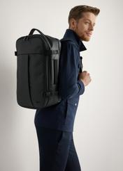 Large black travel backpack TORMN-0409-99(W26) - product view slightly diagonal, on model, against a light background. Knee-length silhouette visible.