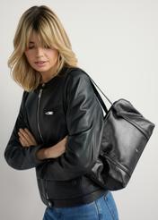 Black women's glossy handbag TOREC-1205-9F(W26) - product view slightly diagonal, on a model against a light background. Half of the silhouette visible.