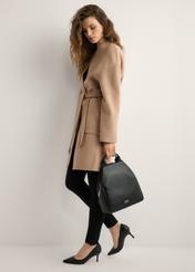 Black women's backpack made of imitation leather TOREC-0923-99(W26), view of the product in the model's hand. Full body visible.