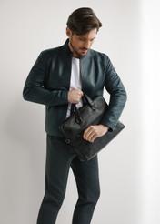 Black leather laptop bag TORMS-0496-99(W26) - diagonal view of the product, held by the model, against a light background. The entire silhouette is visible.