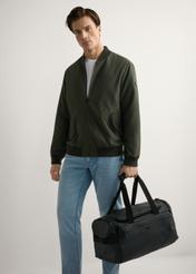 Black TORMN-0412-99(W26) travel bag, product view in model's hand. Full body visible.