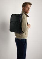 Black men's backpack TORMS-0410-99(W26) - side view of the product, on a model, against a light background. Knee-length silhouette visible.